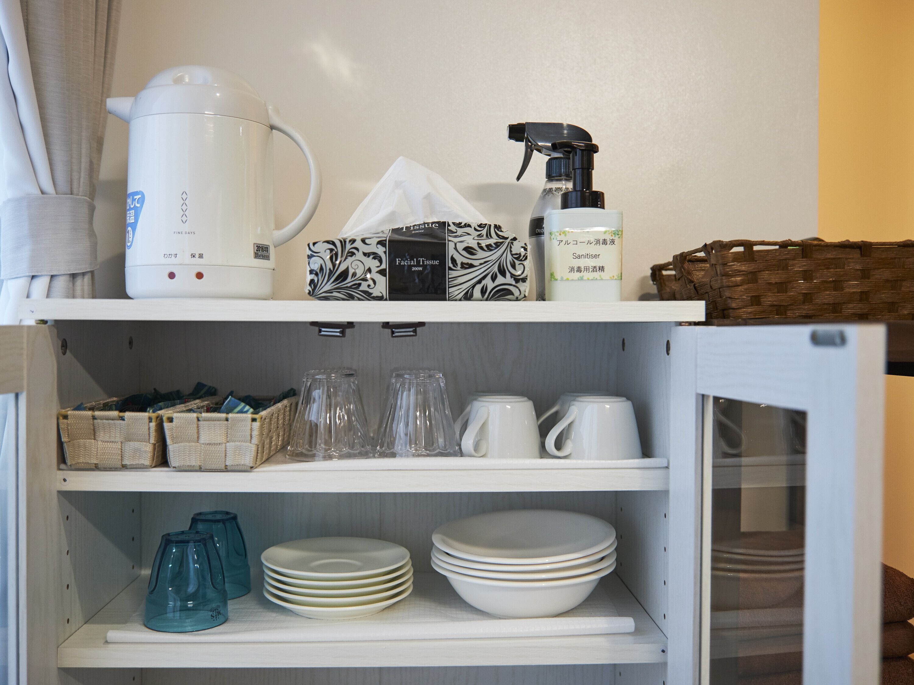 A kitchen with a kettle, facial tissue, a spray bottle, and various glassware and dishes.