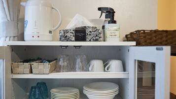 A kitchen with a kettle, facial tissue, a spray bottle, and various glassware and dishes.