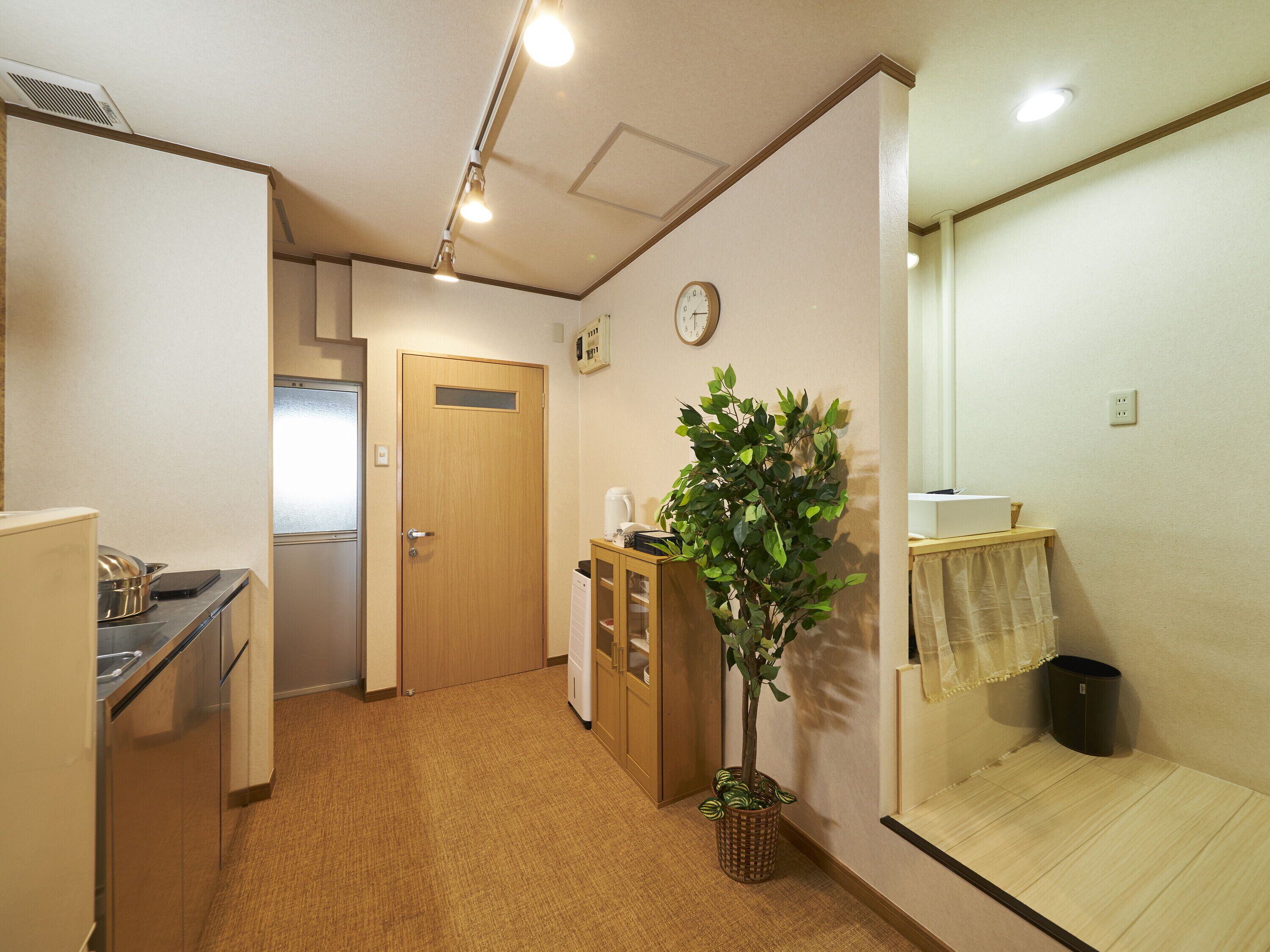 A compact kitchen with a refrigerator, stove, and sink. A wooden door leads to another room. A potted plant is in the corner.