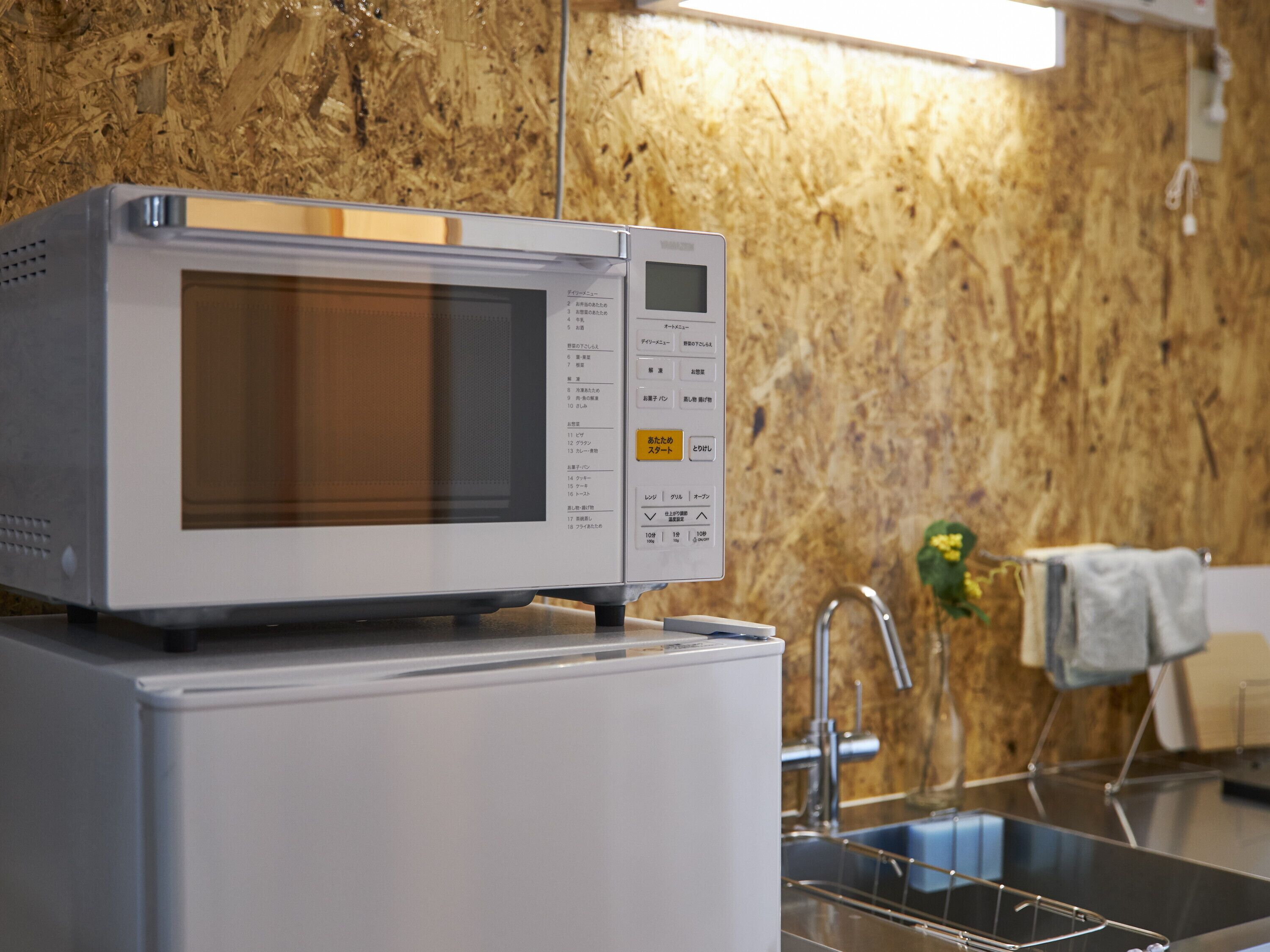 A microwave on top of a refrigerator in a kitchen with a wooden wall and a sink.