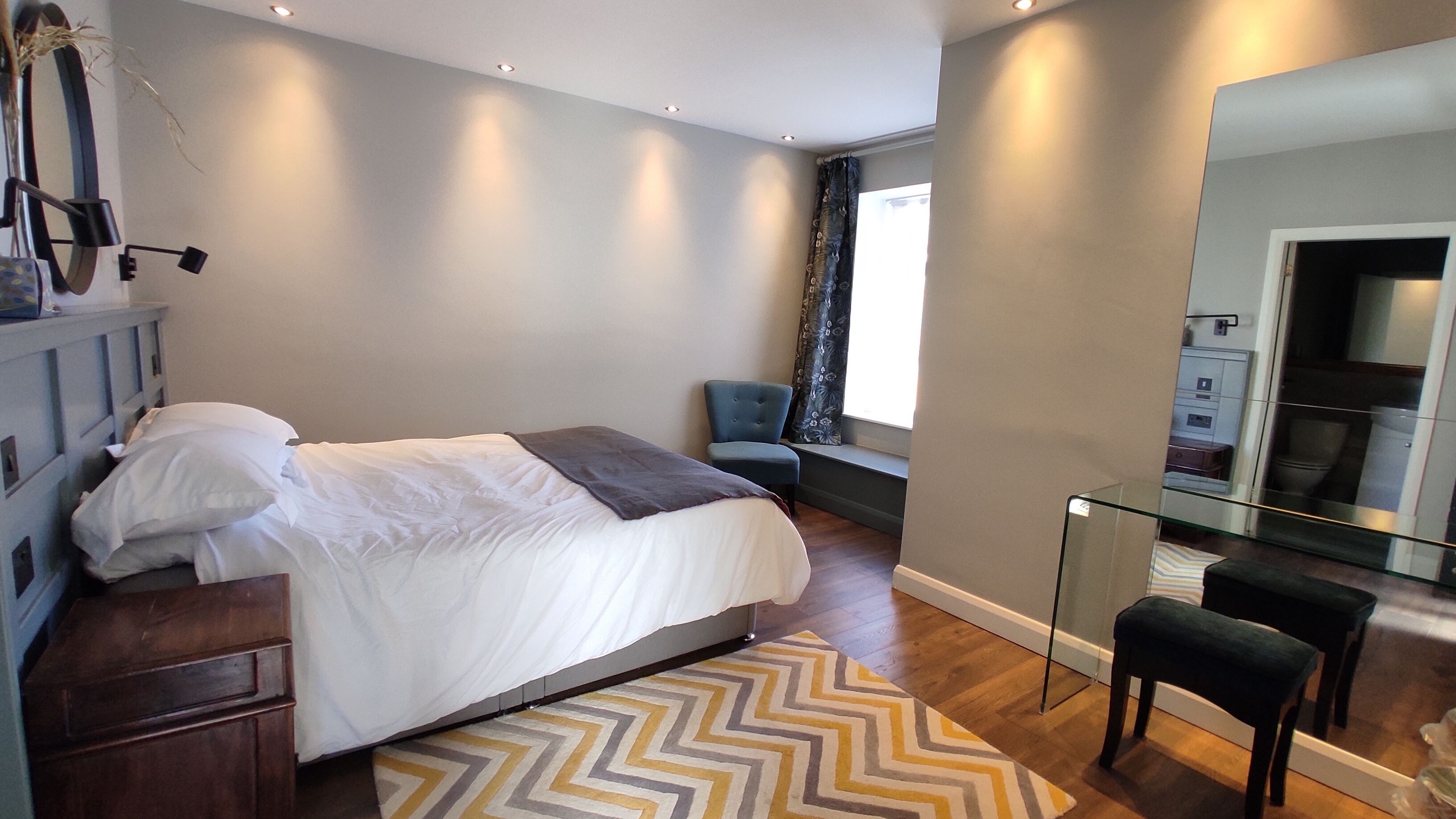 A modern bedroom with a bed, a chair, a desk, and a mirror.