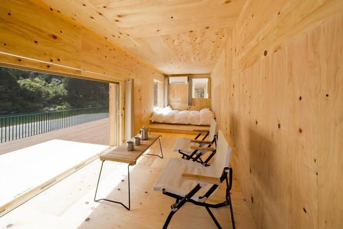 Interior de una cabaña de madera con un ventanal grande, una cama y una mesa de comedor.