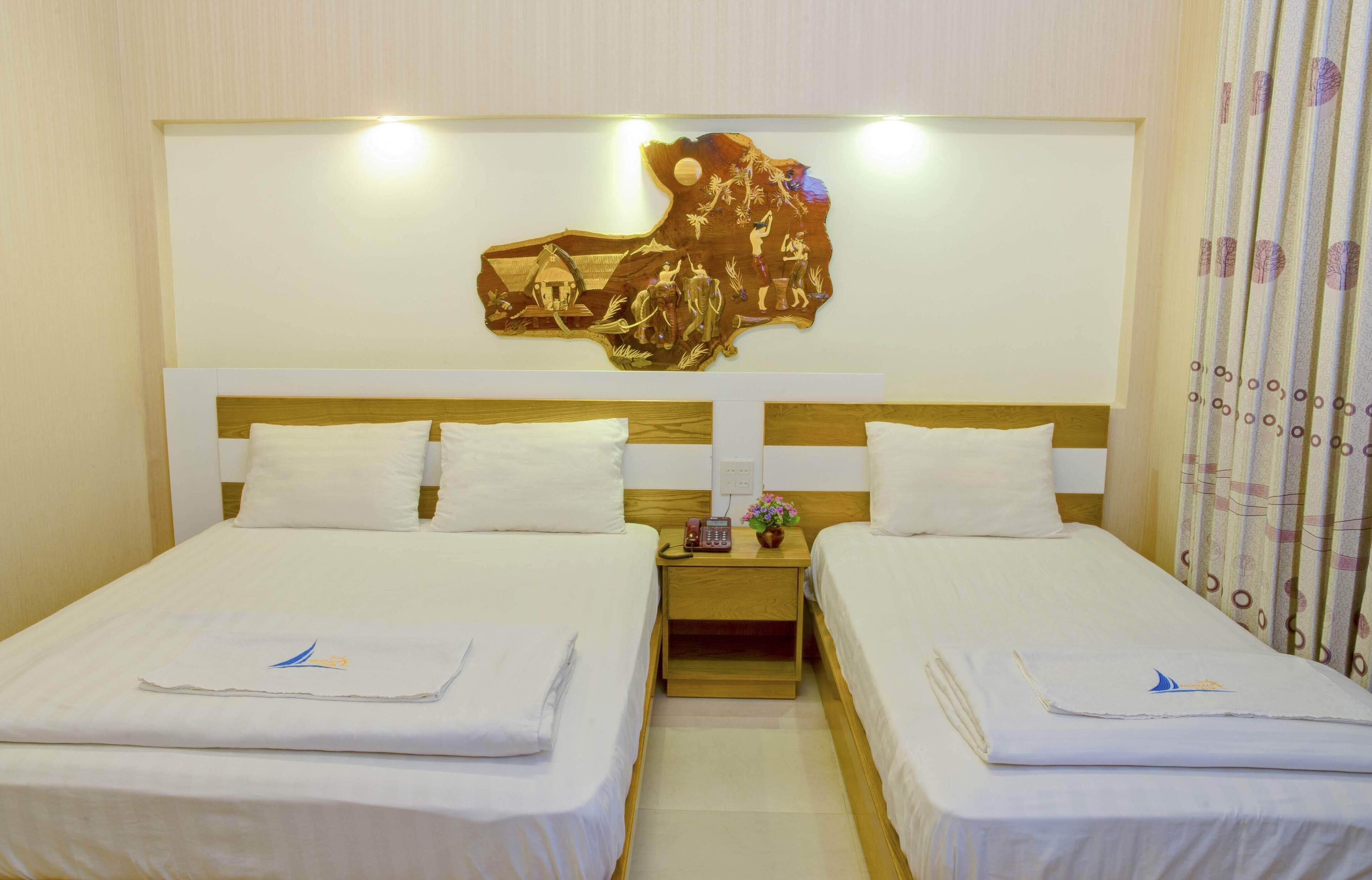 A hotel room with two beds, a wooden headboard, a wall-mounted artwork, and a nightstand with a phone and a vase.
