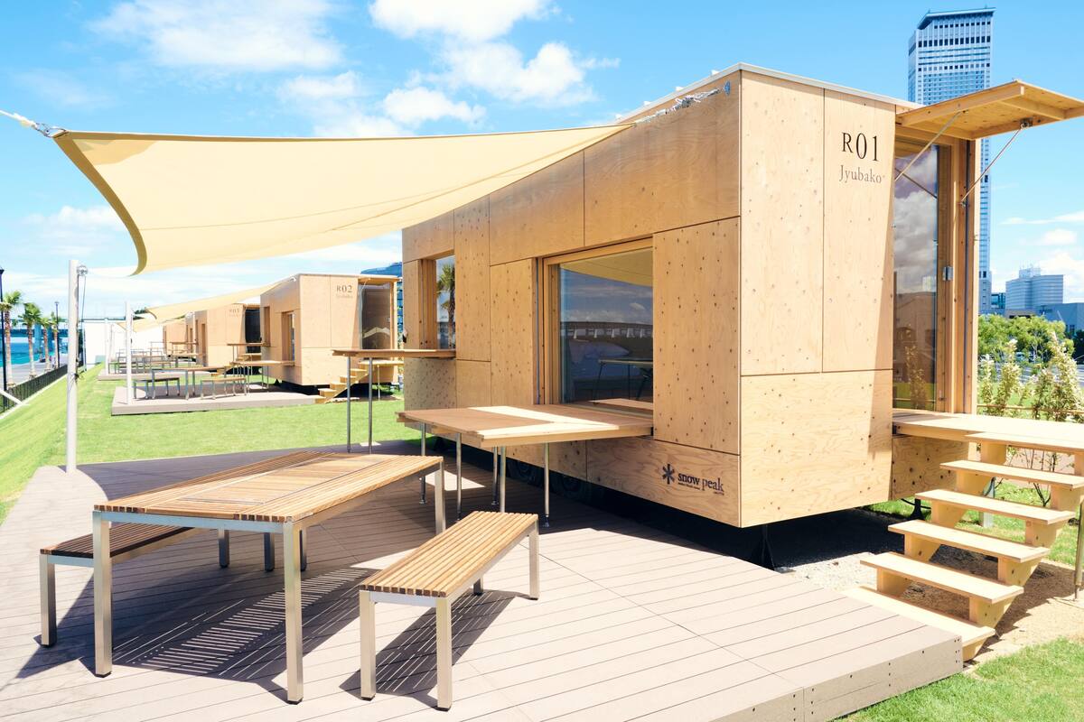 A wooden cabin with a table and benches, a shaded area, and a city view.