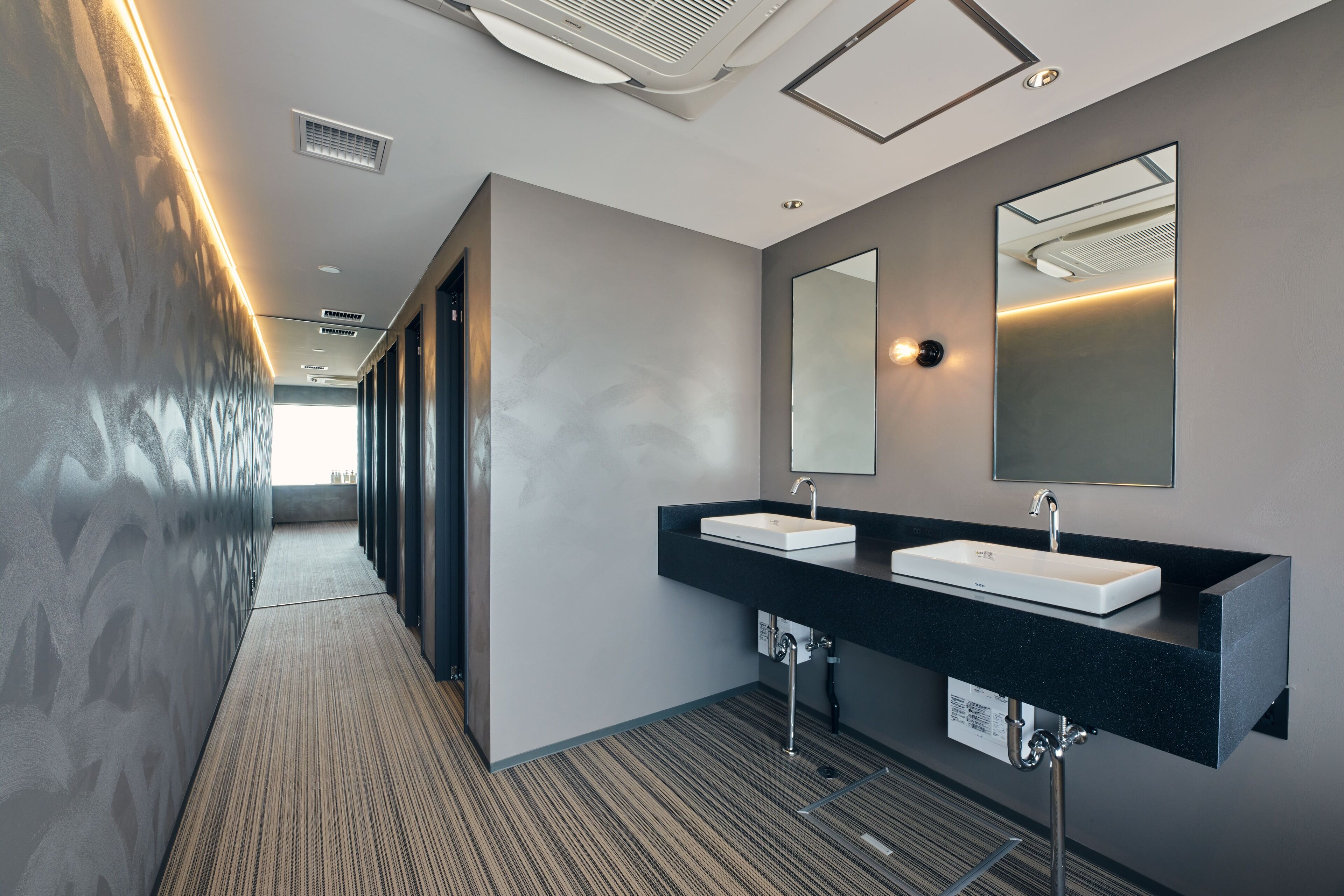 A modern hotel bathroom with two sinks, a large mirror, and a ventilation system on the ceiling.