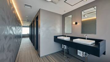 A modern hotel bathroom with two sinks, a large mirror, and a ventilation system on the ceiling.