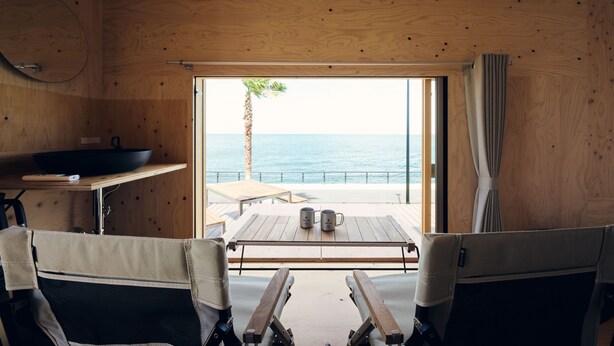 A wooden interior with a view of the sea, a table with two mugs, and two chairs. - Snow Peak Osaka Rinku (Izumisano)