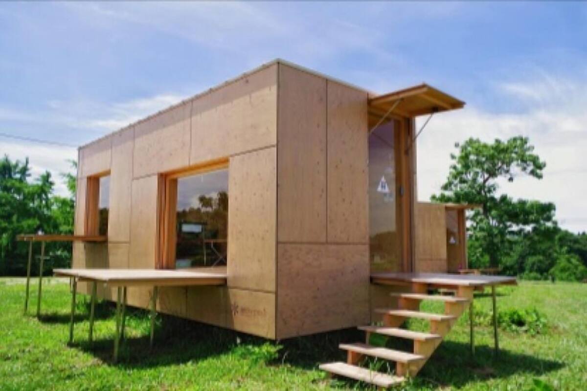 A modern wooden cabin with a flat roof, large windows, and a small porch.