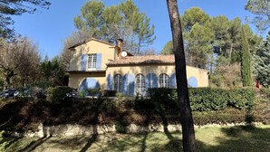 A two-story house with a tiled roof, blue shutters, and a stone wall in front.
