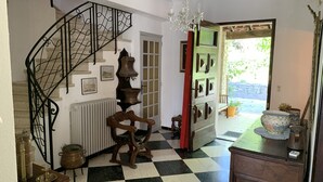 A checkered floor, a staircase with a wrought iron railing, a chandelier, and a door leading outside.