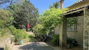A stone-paved courtyard with a pergola, potted plants, and a red umbrella.