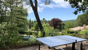 A ping pong table in a garden with trees and a pool in the background.