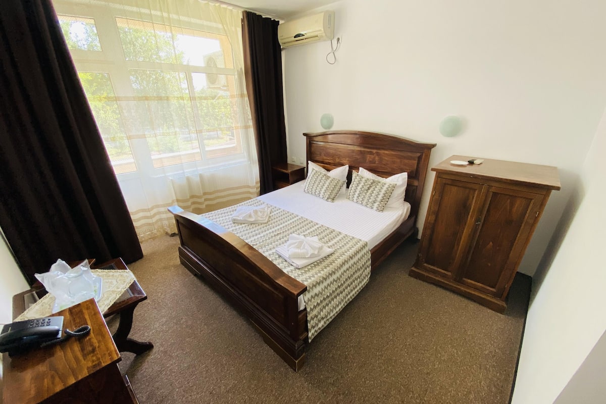 A neatly arranged hotel room with a wooden bed, a bedside table with a telephone, and a small cabinet.