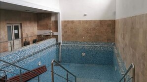 A multi-level indoor swimming pool with blue and beige tiled walls, metal railings, and a bench. - Hotel Ceres (Bala)
