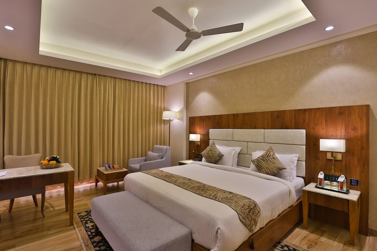 A hotel room with a large bed, bedside tables, a desk, a chair, a ceiling fan, and a window with curtains.