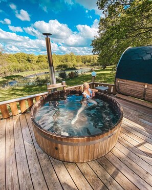 Ein Whirlpool auf einer Holzterrasse mit Blick auf einen See und Bäume.