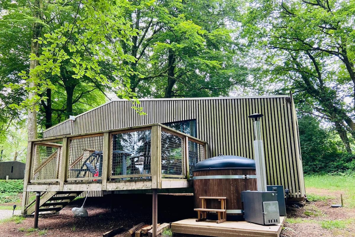 A wooden cabin with a large window, a wooden deck, and a hot tub.