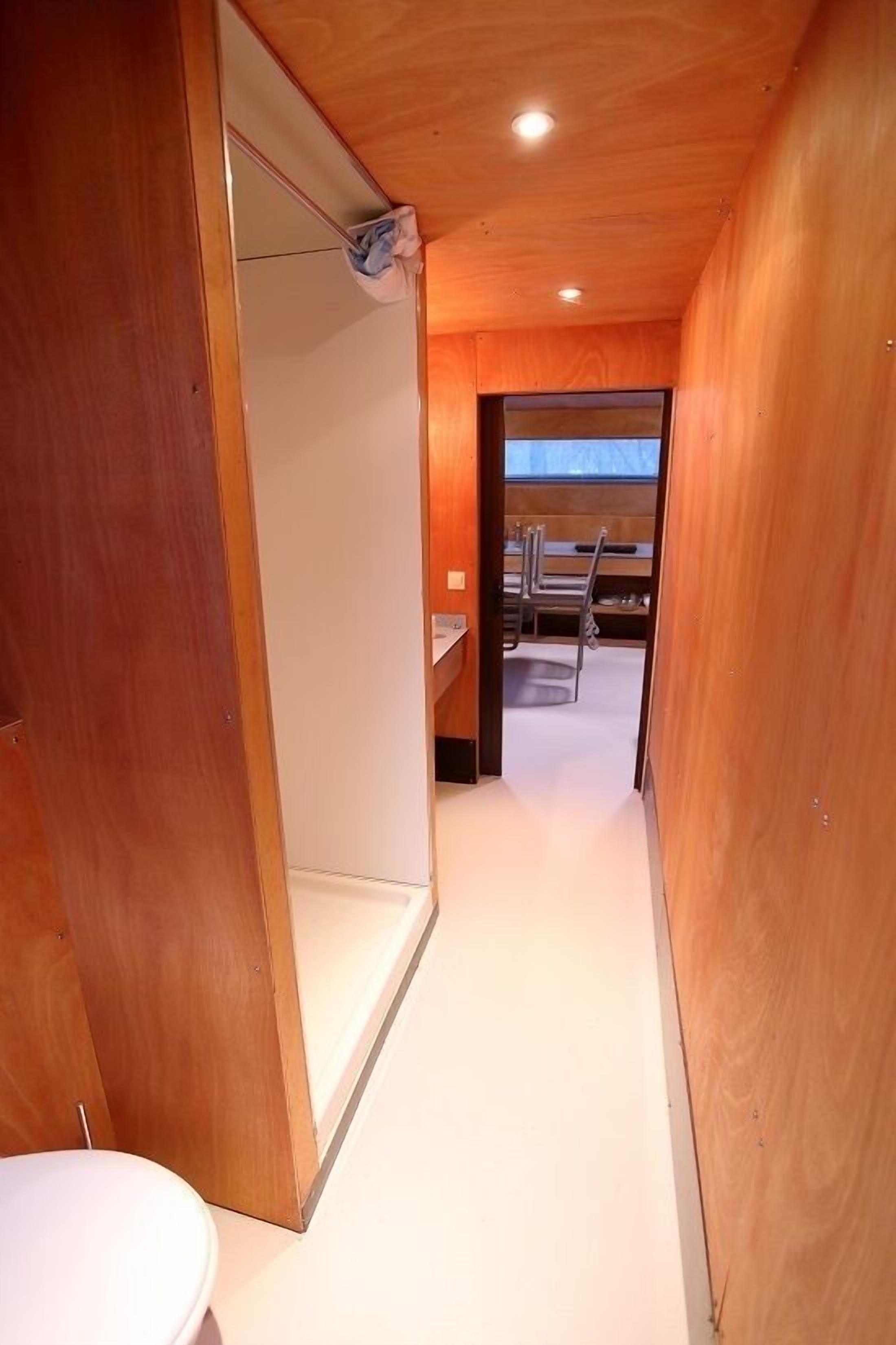 A narrow hallway with wooden walls, a white toilet, and a sink area with a mirror and towel rack.