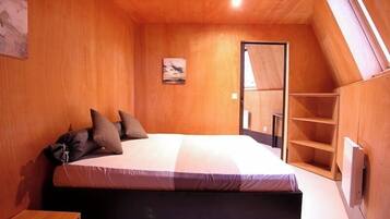 Ein Schlafzimmer mit Bett, Holzwänden, einem kleinen Schreibtisch und einer geneigten Decke.