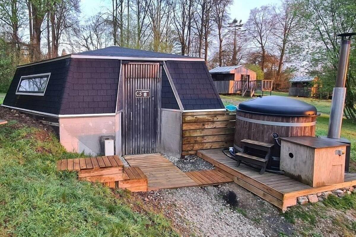 A small, single-story cabin with a sloped roof, a wooden deck, and a hot tub.