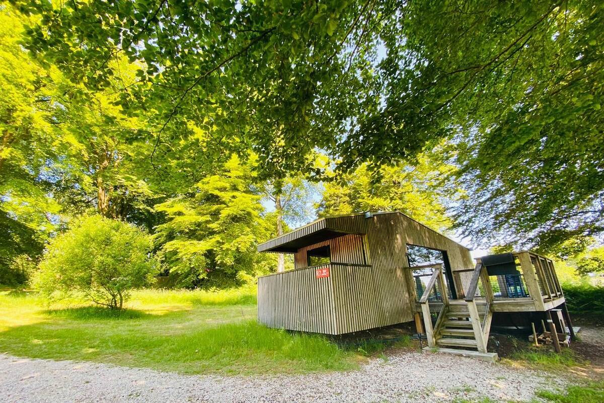A rustic wooden cabin with a sloped roof, surrounded by lush greenery and trees.