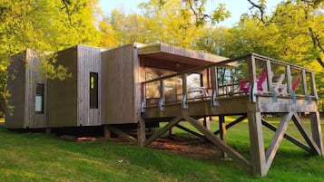 A wooden cabin with a deck and a fenced area.