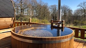 A hot tub on a wooden deck with a metal chimney, surrounded by trees. - Etape en forêt (Noues de Sienne)