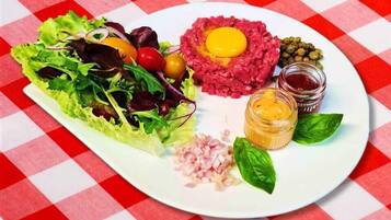 Une assiette comprenant une salade, un jaune d’œuf cru posé sur une base de viande, des cornichons et diverses sauces.