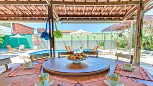 A round wooden table with a fruit bowl, two cups, and a spoon, surrounded by striped placemats and wooden chairs. - Casa com Piscina no Iguape 50m do Mar (Aquiraz)