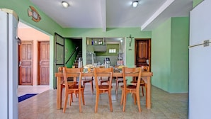 A dining area with a wooden table and chairs, a kitchen in the background, and a clock on the wall. - Casa com Piscina no Iguape 50m do Mar (Aquiraz)