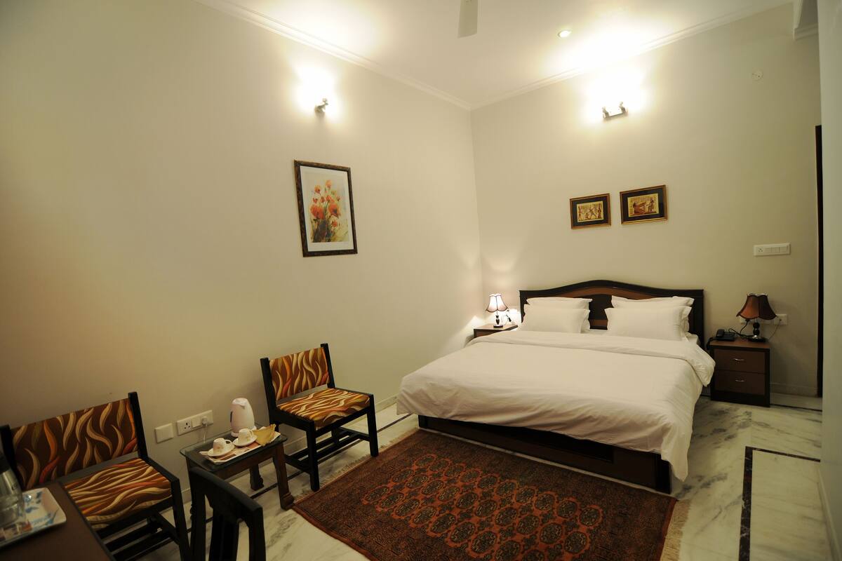 Une chambre d’hôtel comprenant un lit, deux chaises, une petite table, une table de chevet et une lampe fixée au mur.