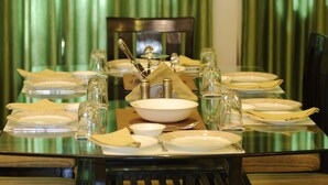 A dining table set with plates, glasses, and cutlery, surrounded by chairs. - Geetanjali Luxury Suites (Jaipur)