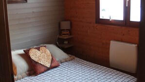 Een slaapkamer met een bed, nachtkastje, lamp, raam met gordijnen en een houten plafond.