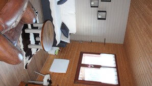 Een kamer met houten vloer, een witte muur met raam, een witte bank en een bruine leren fauteuil.