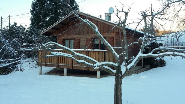 Een houten chalet met een veranda, omgeven door met sneeuw bedekte bomen en een heldere lucht.