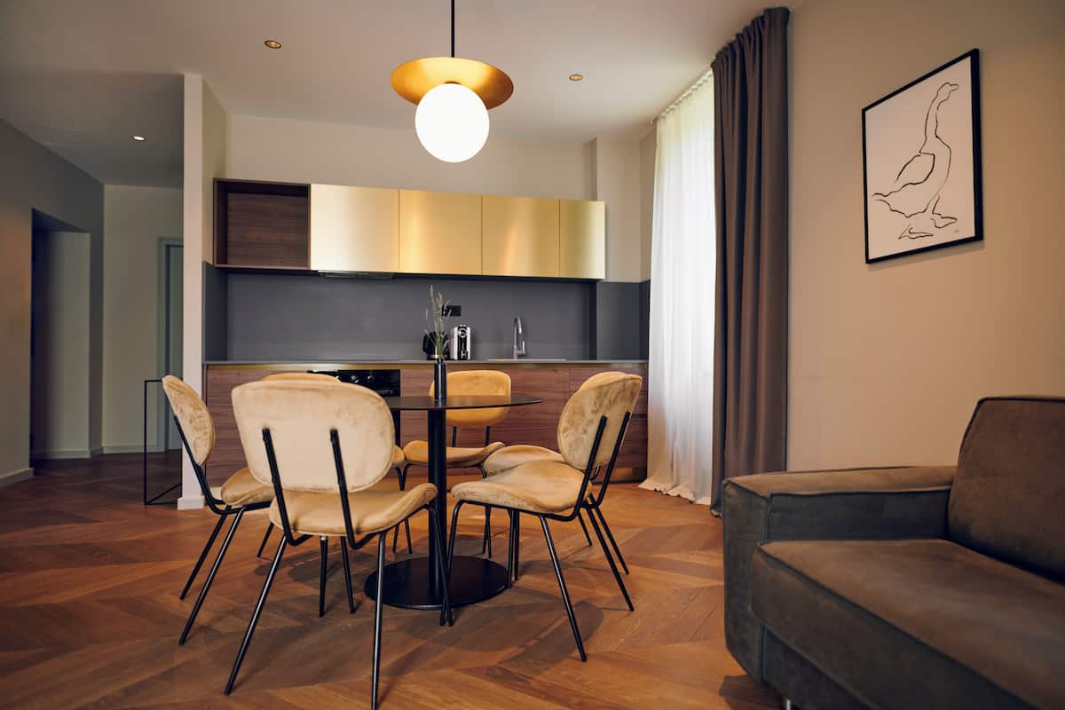 A modern living room with a round dining table, four chairs, a sofa, and a kitchen in the background.