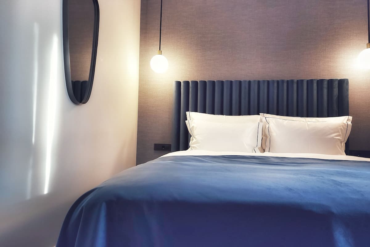 A modern hotel room with a large bed, a round mirror, and two pendant lights.