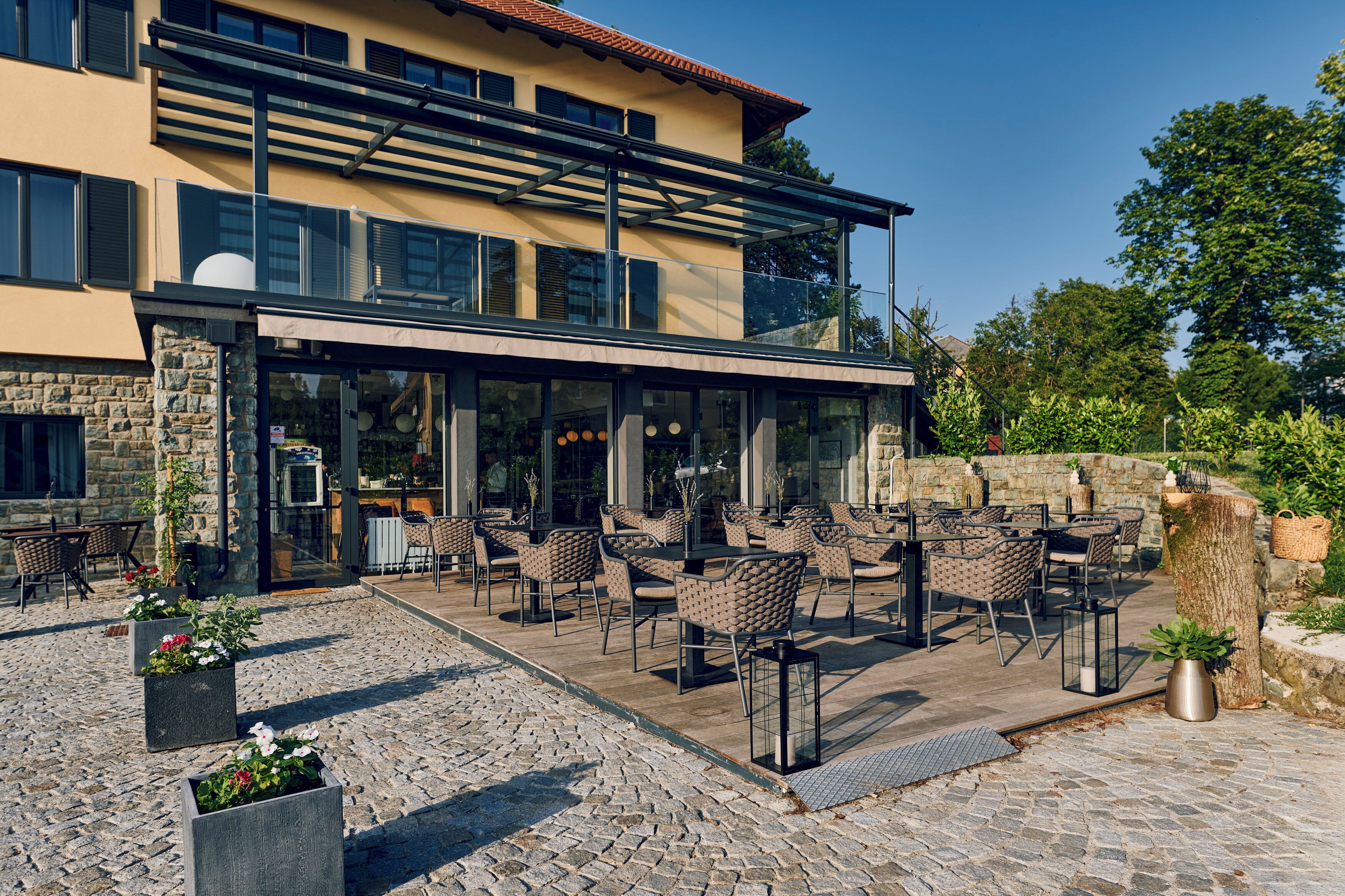 A modern building with a glass facade, outdoor seating area with wicker chairs, and a stone wall.