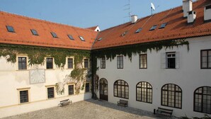 Ein Innenhof mit gefliestem Boden, ein weißes Gebäude mit Rundbogenfenstern und ein rotes Ziegeldach.