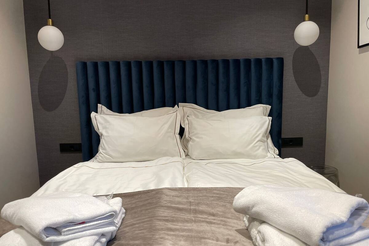 A neatly made bed with white linens and pillows, a dark blue headboard, and two white towels on the bed.