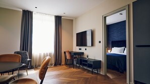 Ein Hotelzimmer mit Holzdielen im Fischgrätmuster, einem Schreibtisch mit Stuhl, einem an der Wand montierten Fernseher und einem Bett mit dunklem Kopfteil.
