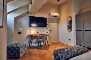 A modern bedroom with a wooden floor, a desk with a chair, a bed, a TV mounted on the wall, and a wardrobe.