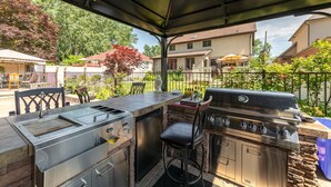 Un área de cocina al aire libre con una parrilla, un lavamanos y taburetes de bar.