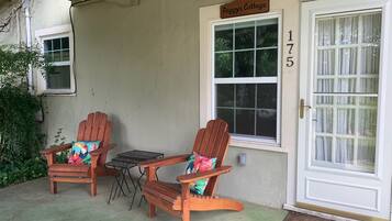 A porch with two wooden Adirondack chairs, a small table, and a door labeled 'Peggy's Cottage.'