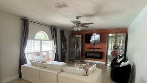 A living room with a sectional sofa, a ceiling fan, a TV, and a fireplace. - Mi Casa Es Su Casa!!🏡 4 Bdrm home with pool (Orlando)
