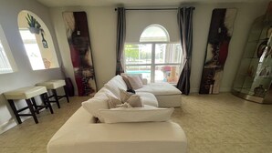 A spacious living area with a large white sofa, a small round table, and a glass elevator. - Mi Casa Es Su Casa!!🏡 4 Bdrm home with pool (Orlando)