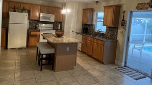 A spacious kitchen with a central island, wooden cabinets, a refrigerator, and a microwave. - Mi Casa Es Su Casa!!🏡 4 Bdrm home with pool (Orlando)