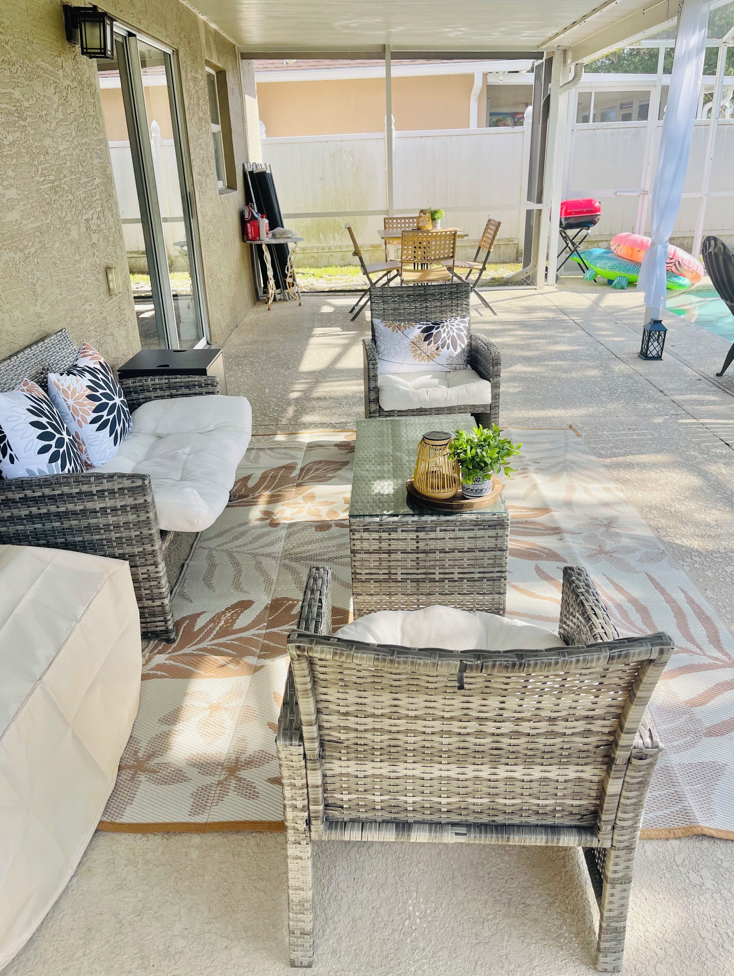 Un'area patio esterna con mobili in vimini, tra cui divani e poltrone, un tavolo con una pianta e una zona coperta con vista sul giardino.
