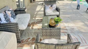 Un'area patio esterna con mobili in vimini, tra cui divani e poltrone, un tavolo con una pianta e una zona coperta con vista sul giardino.