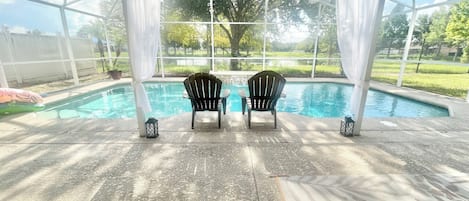 An indoor pool area with two chairs facing the pool, a covered patio, and a view of the outdoors.